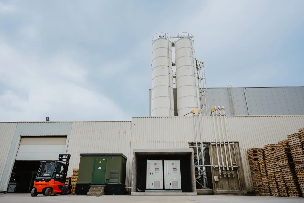 Batterijkasten naast een productiehal met heftruck en materiaal