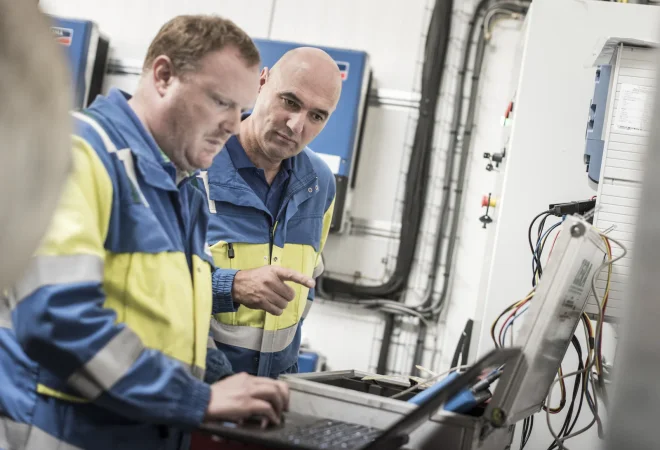 Twee technici in werkkledij controleren een PV-installatie met een laptop