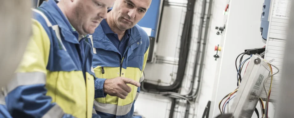 Twee technici in werkkledij controleren een PV-installatie met een laptop