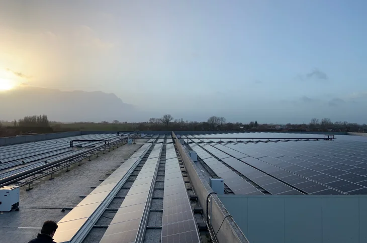 Rijen zonnepanelen op een industriedak bij zonsopgang