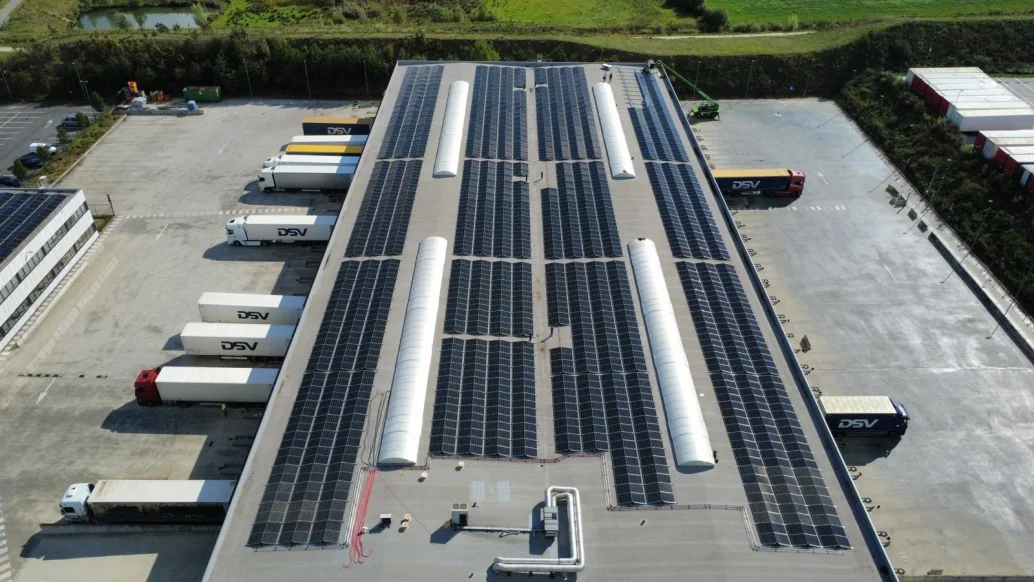 Luchtfoto van het platte dak van het logistieke centrum van DSV in Rekkem, belegd met zonnepanelen boven de laad- en loskades