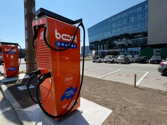 Oranje Boostcharge DC-snellader op de parking van de Planet Group Arena in Gent, met het stadion op de achtergrond