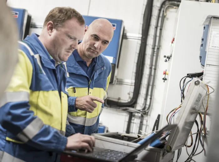 Twee technici in werkkledij controleren een PV-installatie met een laptop