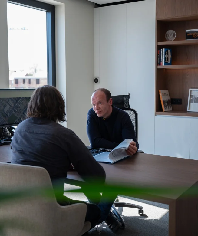 Twee medewerkers in gesprek aan de vergadertafel in het kantoor van Batimont