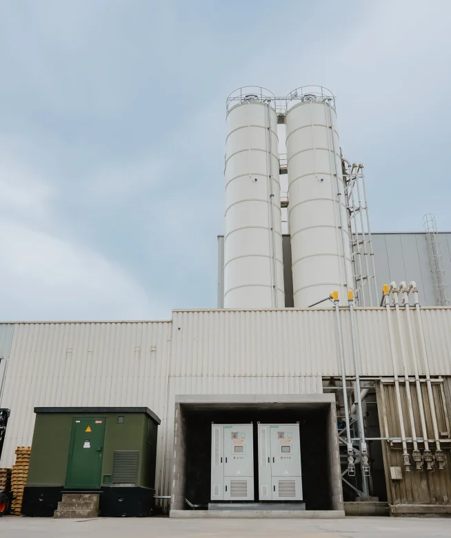 Batterijkasten naast een productiehal met heftruck en materiaal