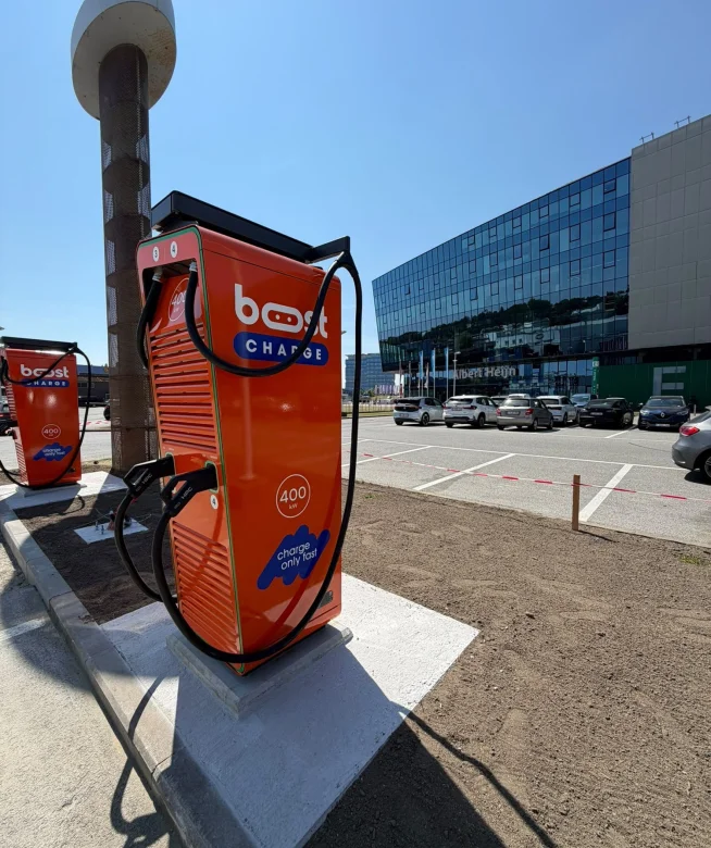 Oranje Boostcharge DC-snellader op de parking van de Planet Group Arena in Gent, met het stadion op de achtergrond