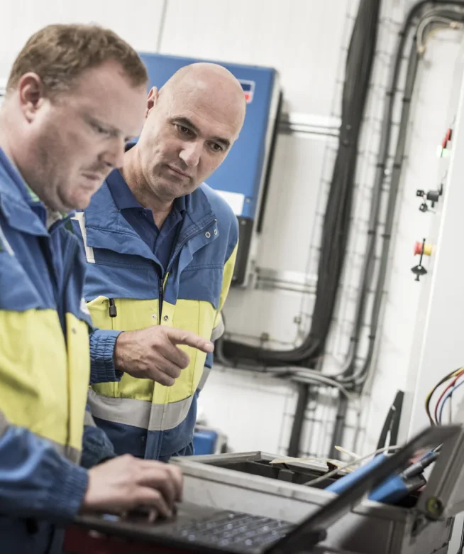 Twee technici in werkkledij controleren een PV-installatie met een laptop